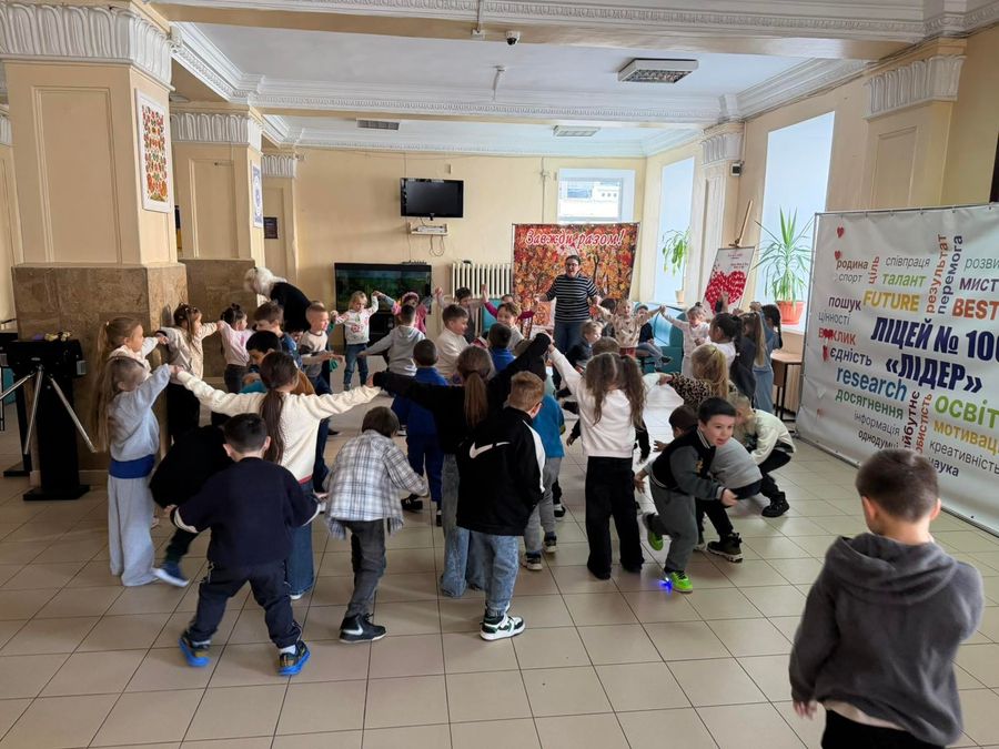Діти в колі біля банера ліцею присідають під час рухливої гри